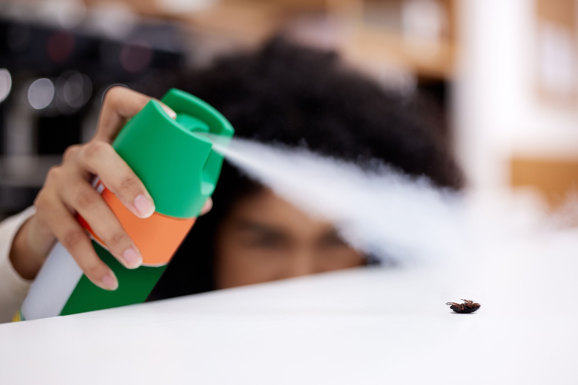 Shot of a young woman spraying an insect on a counter at home